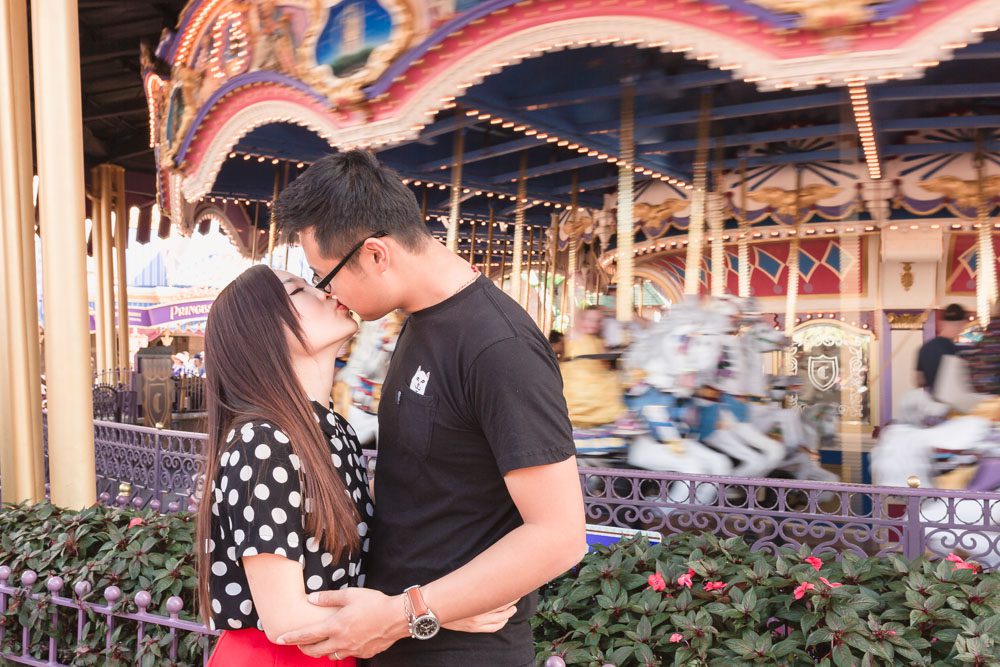 Married couple kisses in front of the spinning carousel for a creative anniversary engagement session photo at Disney