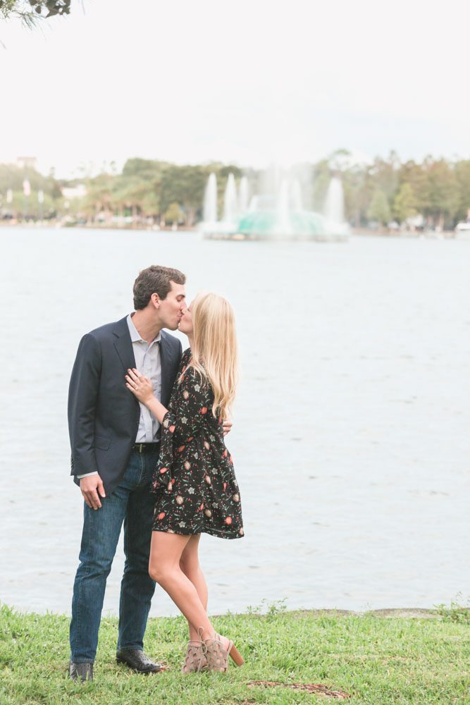 Newly engaged couple kisses in front of the fountain at Lake Eola in downtown Orlando after their surprise proposal is captured by top Orlando photographer