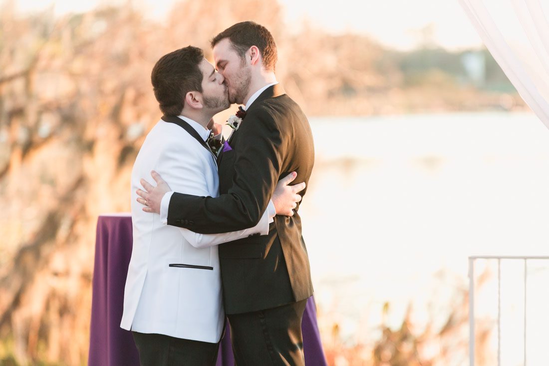 Grooms share their first kiss during a gay wedding in Orlando at the Cypress Grove Estate House at sunset on the lake