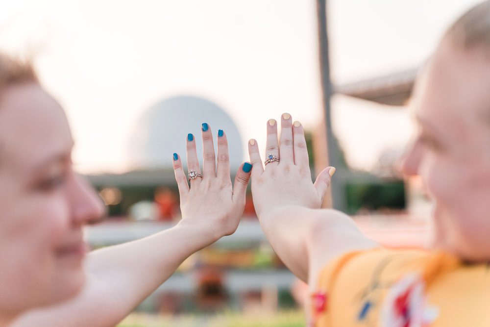 Close up of the bride's engagement rings in front of Spaceship Earth in Epcot during their same sex engagement photography session with top Orlando gay wedding photographer