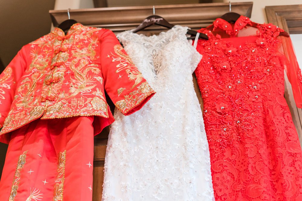 Traditional chinese and vietnamese red dresses hung alongside white wedding dress during an Asian wedding in Oklahoma City captured by Orlando wedding photographer